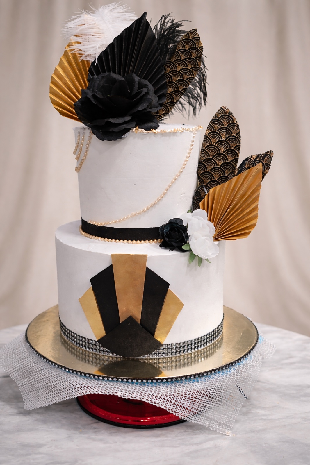 Two-tier art deco cake in black, white and gold with gold palm fans and a sugar rose